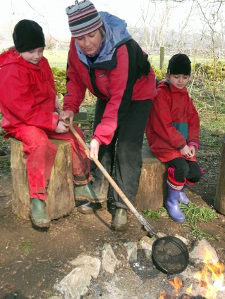 Adult and 2 children making popcorn over a fire (onsite ground-based) at Thornbridge Outdoors