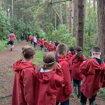 School children wearing goggles and red cagoules walk the Night Line in the woods at Thornbridge Outdoors