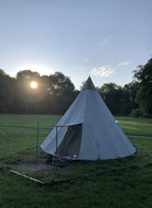 Teepee at dawn with the sun rising through the trees