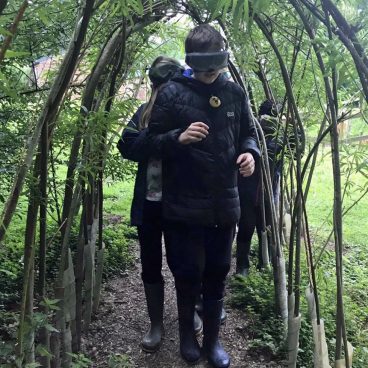 Children walk beneath a willow archway with Night Line goggles on, unable to see