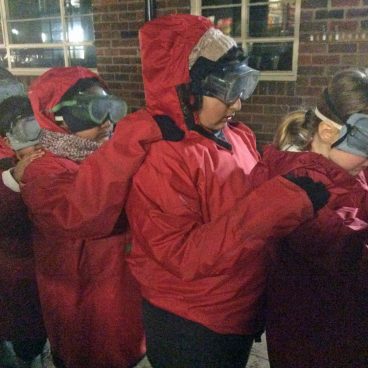 Students hold onto eachother's shoulders as they stand in a line wearing big coats and goggles for the Night Line challenge under the cover of darkness