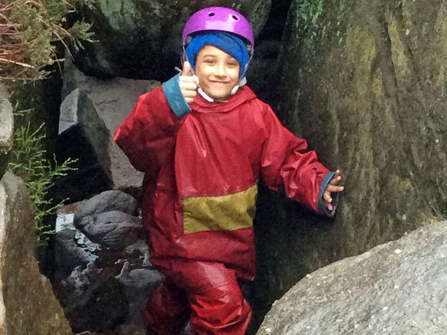 School child gives the camera and smile and a thumbs up as he clambers between boulders on a weaselling session in the Peak District