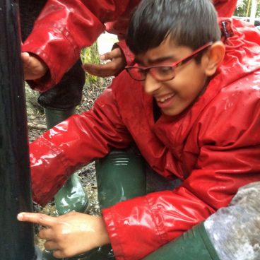 Student in a soaked cagoule grins while taking part in a team problem solving challenge