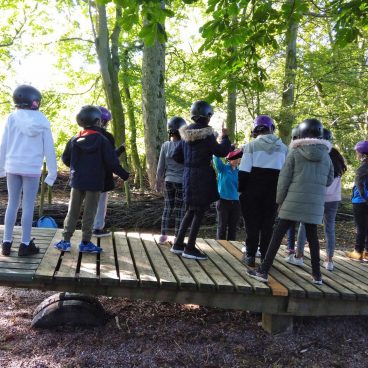 Children stand on the see saw at Thornbridge Outdoors and listen to the instructor's instructions