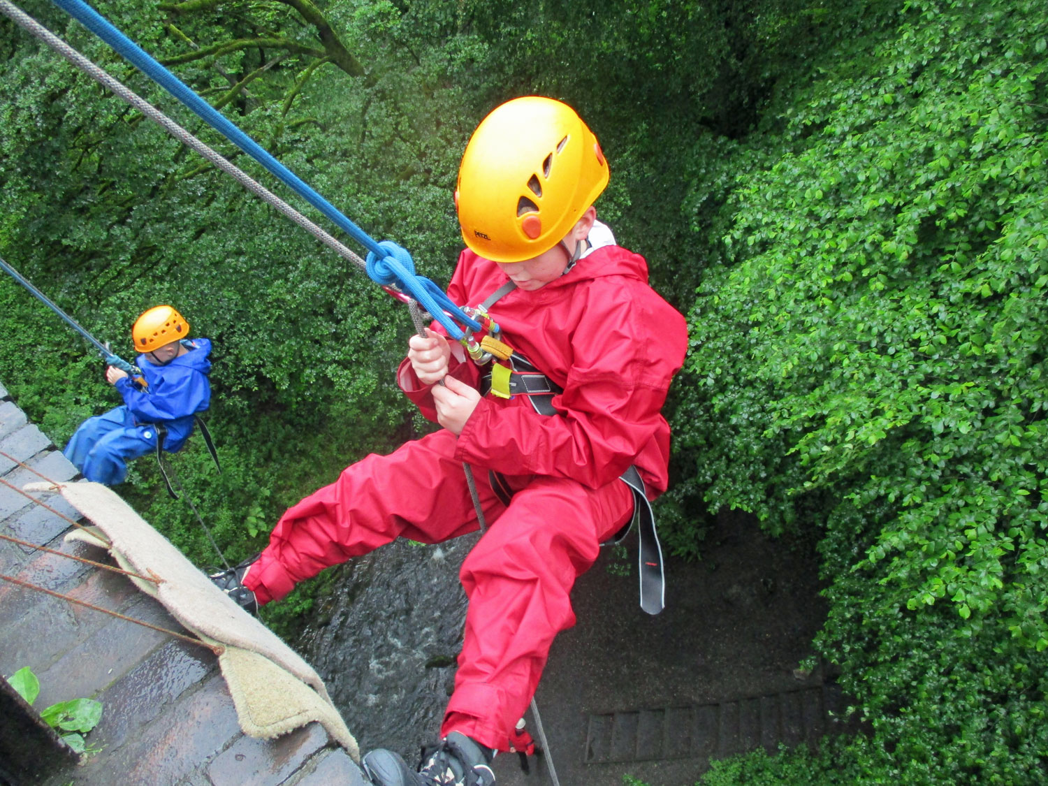 Two school boys abseil over the edge of a bridge supported by ropes from above