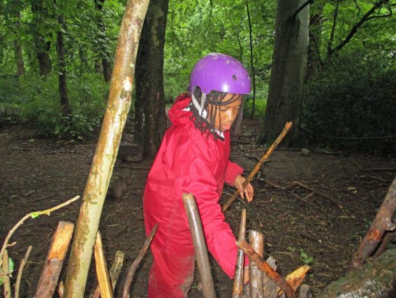 A school child builds a den from sticks in the woods