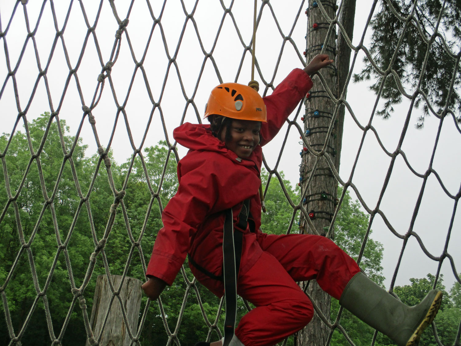 Small boy grins while dangling from his support rope after finishing his cargo net climb