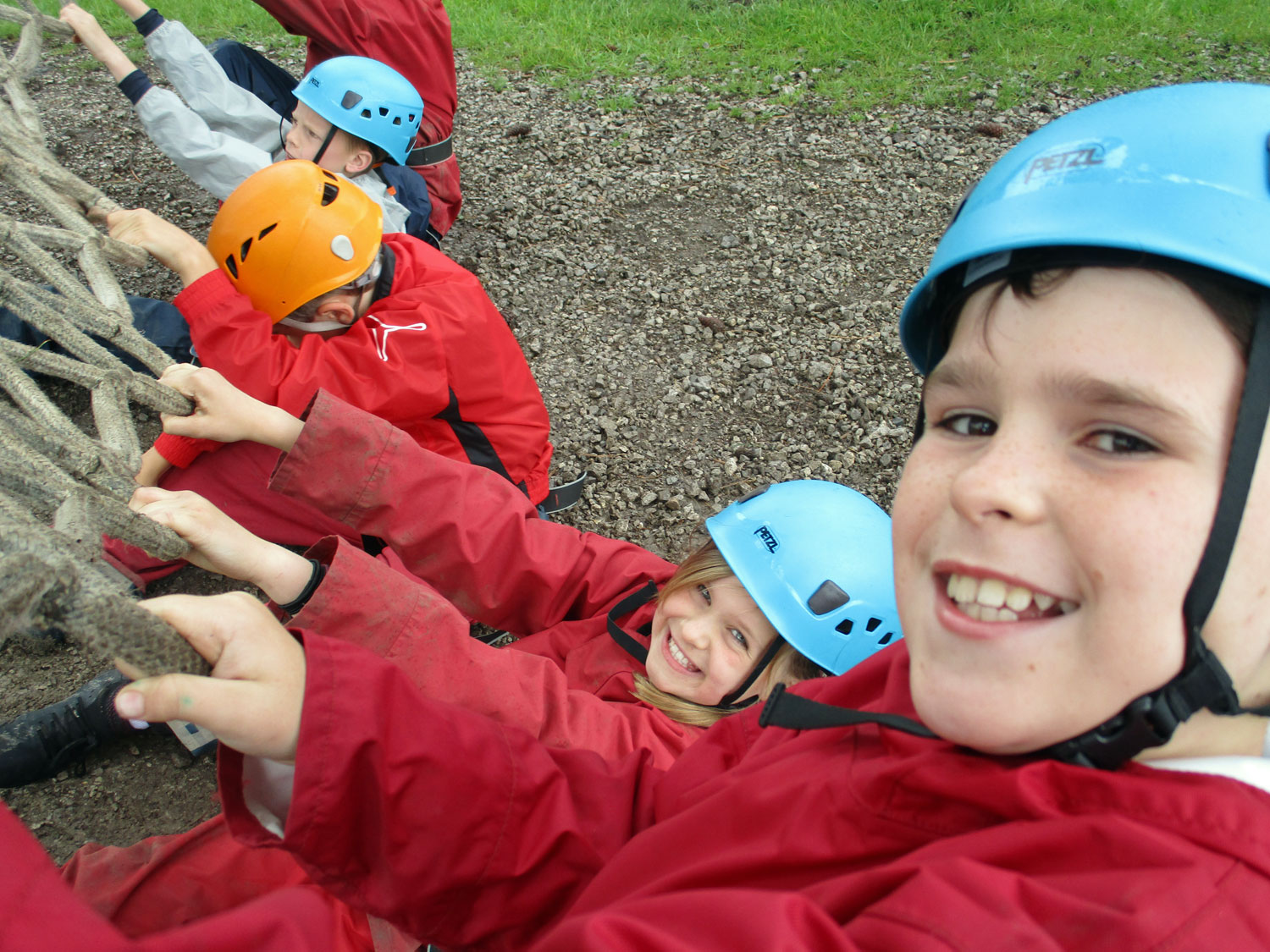 School children grin as they pull on the bottom of the cargo net to help their classmates as they climb up above