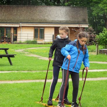 Two school girls work together to walk on two wooden planks across the field