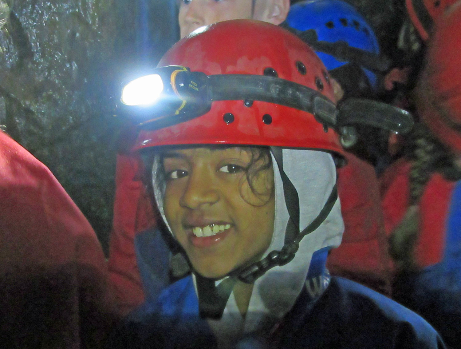 School girl smiles inside a cave with the headtorch on her helmet lit