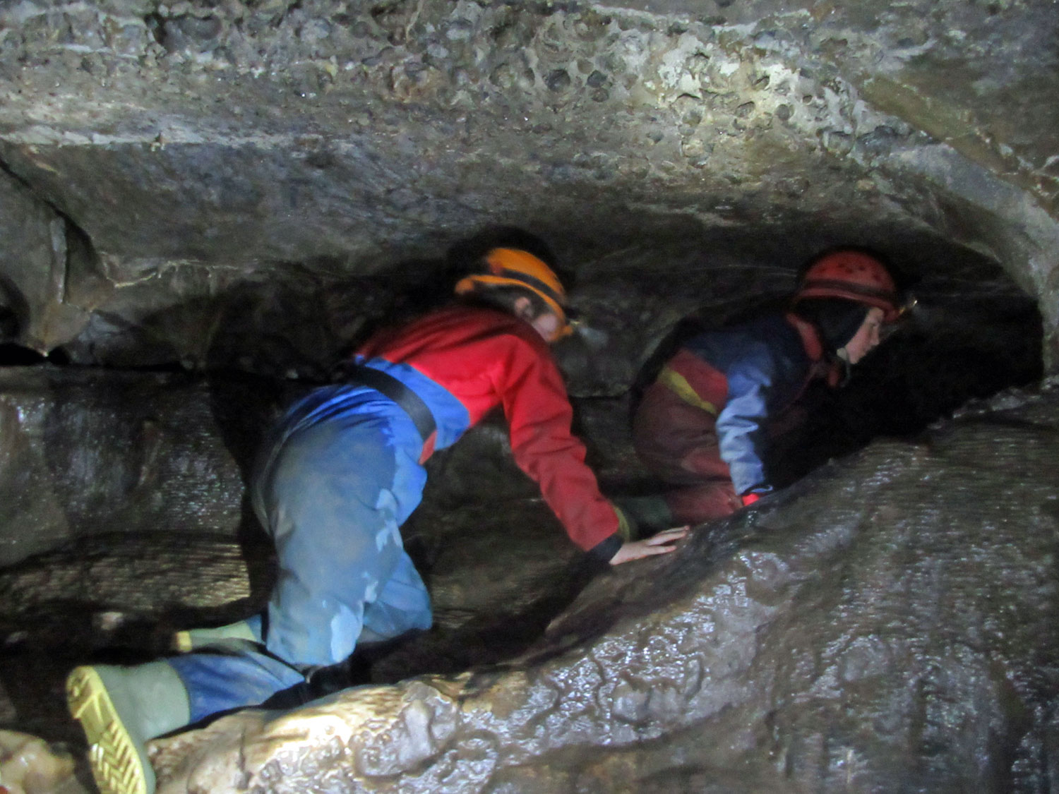 School children clamber through a narrow gap in a cave