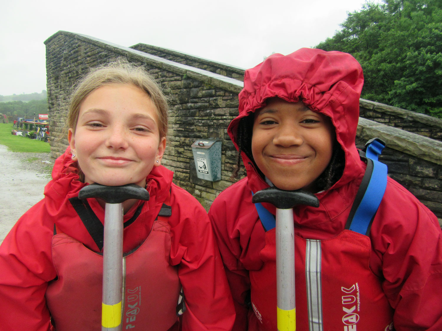 Two school girls smile and pose with their canoe paddles