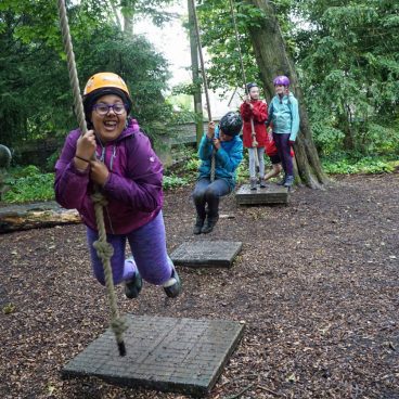 Four students swing on the low rope course in the woods