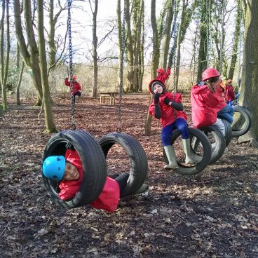 Children swing from tyres on the low rope course and smile for the camera