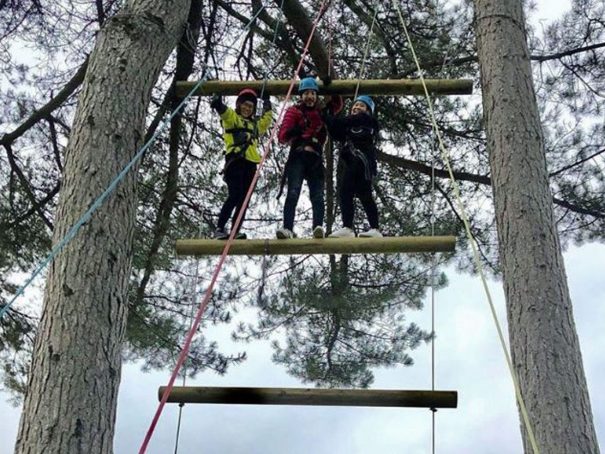 Three students stand atop the Jacob's ladder smiling as they've made it to the highest rung