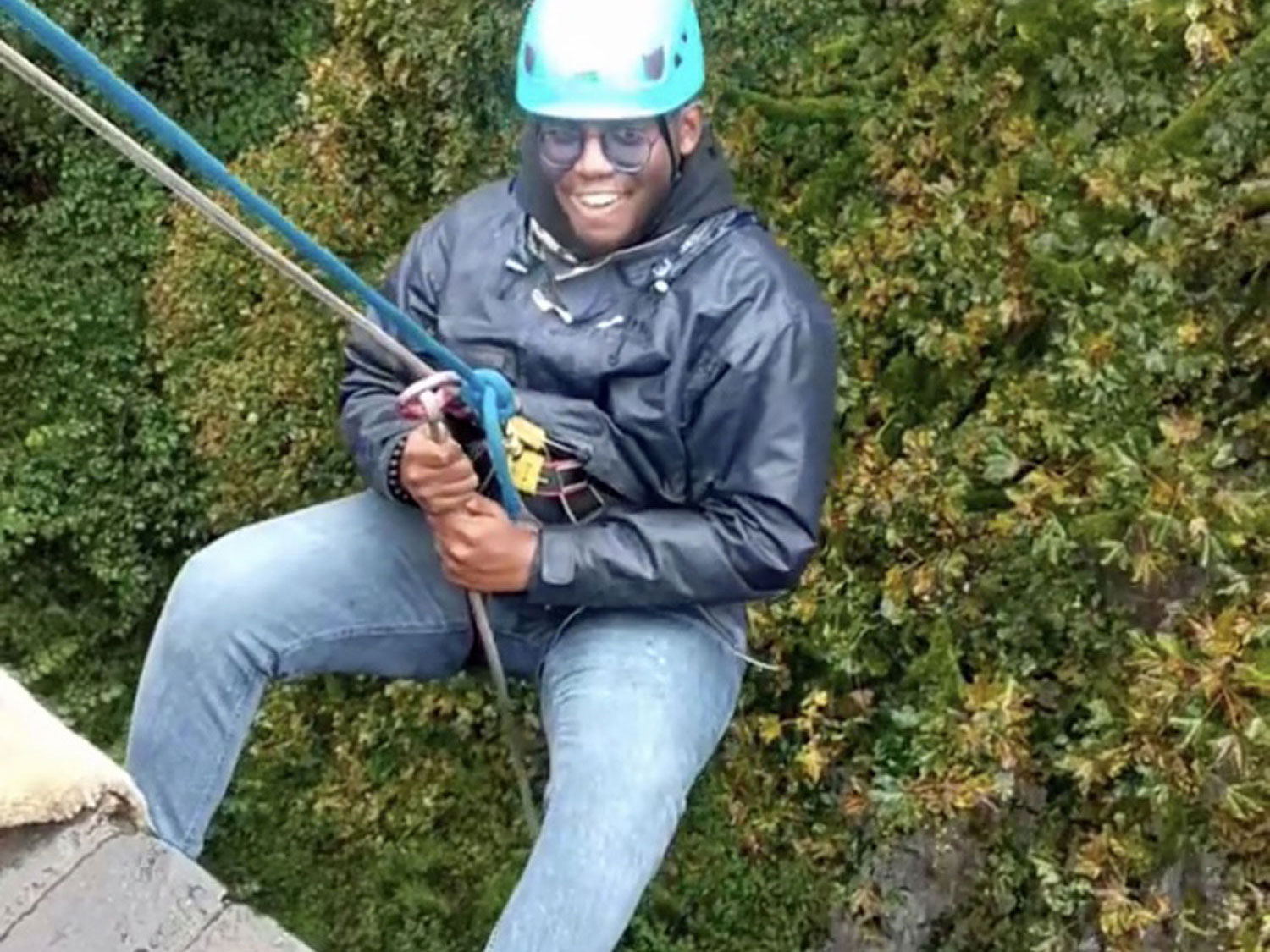 Smiling man leans back over the edge of the bridge, he's supported on a rope during an abseiling session